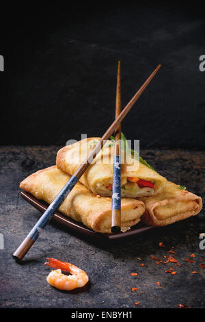 Fried spring rolls with vegetables and shrimps, served on squer ceramic plate with chopsticks over black background. Stock Photo