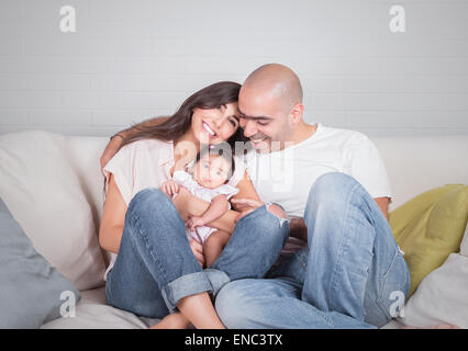 Portrait of happy cheerful family sitting on the couch at home, young parents enjoying time spent with their adorable daughter Stock Photo