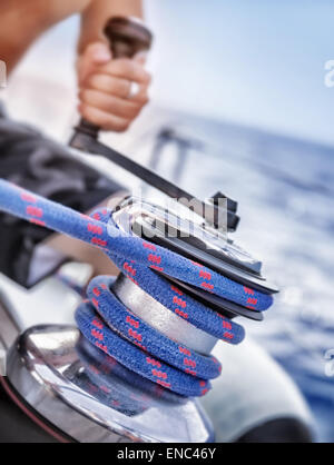 Holder of rope on sailboat, man pulling handle of spool, macro photo of yacht detail, working on water transport, luxury summer Stock Photo