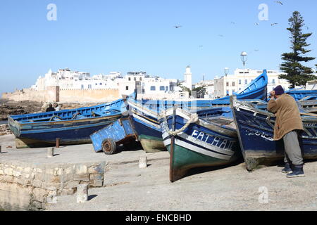 A Berber fisherman rests on boats in the harbour of the coastal town of Essaouira, Morocco Stock Photo