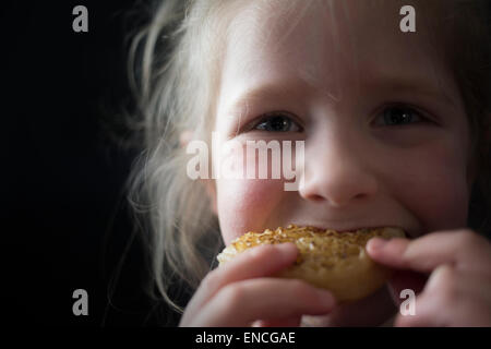 Five year old young girl eating a crumpet on a black background. Facing camera. Stock Photo