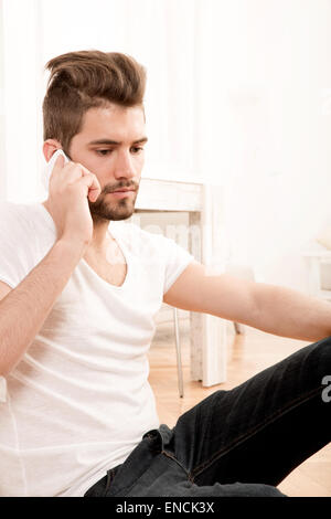 Portrait of an attractive man sitting on the floor using mobile phone. Stock Photo