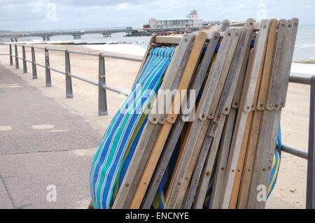 A stack of deck chairs resting up against some railings. Bournemouth pier is in the background. Stock Photo