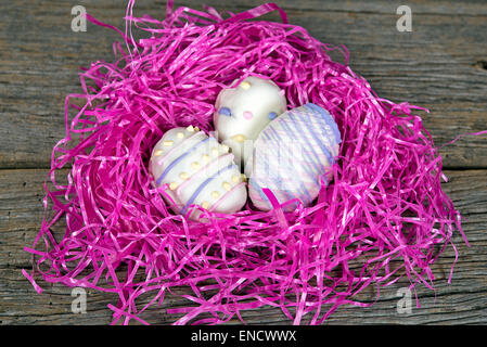 Decorative Easter egg cookies in bright pink grassy nest on rustic wood. Stock Photo