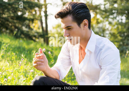 Attractive young man touching flowers in a forest Stock Photo