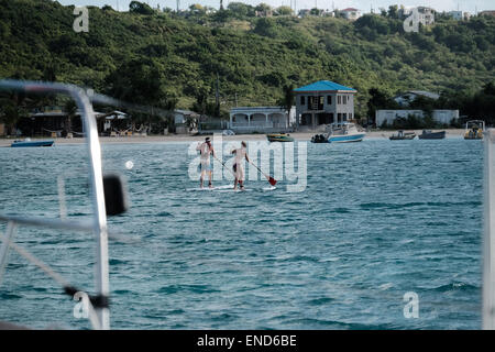 Two people paddleboarding from their yacht to the beach Stock Photo