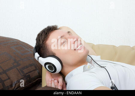 Handsome man with headset listening to music smiling lying on couch relaxing Stock Photo