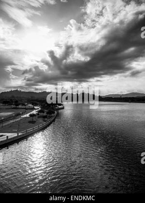 Black and white image of a lake with the sun shining behind clouds Stock Photo