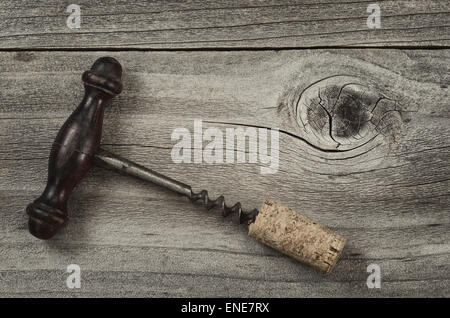 Vintage concept of an old corkscrew with attached cork on rustic wooden boards. Stock Photo