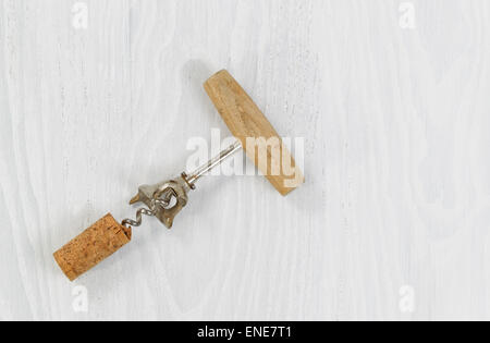 Top view of an antique corkscrew with cork attached on white wood. Stock Photo