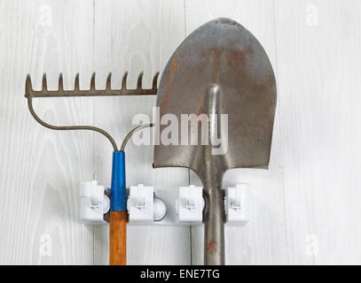 Close up image of garden tools hanging from rack on white wood. Stock Photo