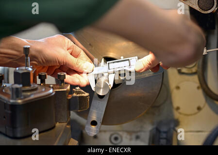 Hands of a male mechanical engineer while measuring a metallic piece with an accurate caliper, at workbench Stock Photo