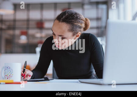Portrait of young woman working at her desk. Busy african woman taking notes. Stock Photo