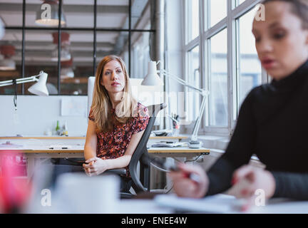 Image of young woman sitting at her desk looking away thinking. Female executive in office lost in thought. Stock Photo