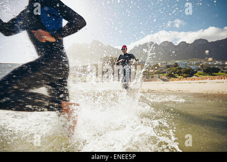 Image of triathletes rushing into the water. Athlete running into the water, training for a triathlon. Stock Photo