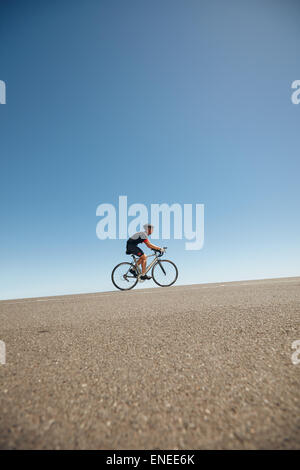 Image of male cyclist riding bicycle up hill. Athlete training for cycling event of a triathlon competition. Stock Photo