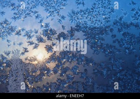 Ice snowflakes and frost pattern over the sun on frozen Christmas winter window at sunset. Blue color background Stock Photo