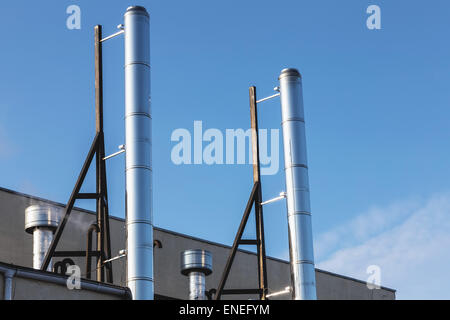 Smoke metal pipes on rooftop of industrial building against blue sky background Stock Photo