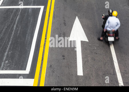 Street detail with scooter biker, yellow line and arrow road markings Stock Photo
