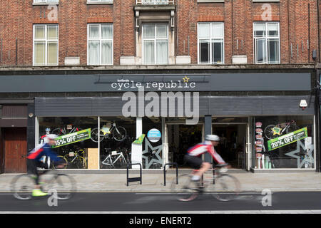 two male cyclists seen in blurred motion pass branch of cycle republic in twickenham, middlesex, england Stock Photo