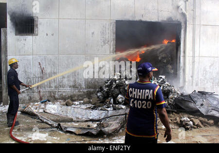 Fire fighters extinguishing from burning garments factory building while heavy smoke fire flame rises from burning goods after fire broken out incident due electric short circuit at chemical warehouse of garments factory at SITE area in Karachi on Monday, May 04, 2015. At least 12 workers were injured as a garment factory caught fire in SITE area of Karachi. All the fire tenders of city are called to extinguish the fire which has been termed 'Level 3' by the firefighting authorities. Stock Photo