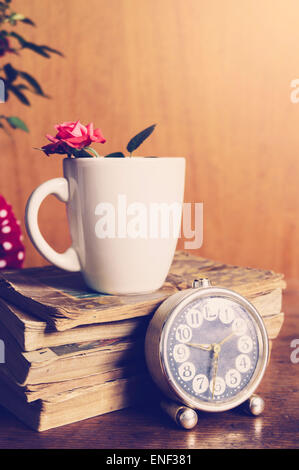Cup, books and flowers on wooden background. Romantic setting in natural light Stock Photo