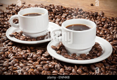 Two coffee cups among coffee beans on a wooden table. Stock Photo