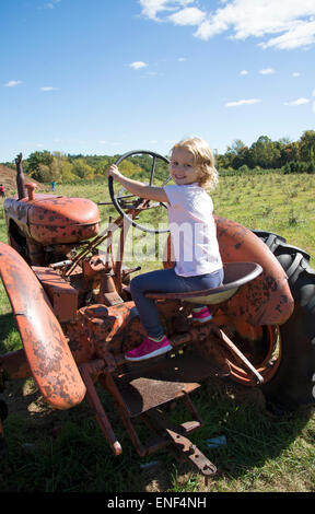 Little girl playing on an old rusty red farm tractor Child steering a vehicle Stock Photo