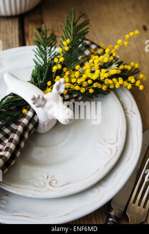 Spring festive dining table setting with yellow mimosa flowers, candles, napkins and vintage cutlery on a wooden board Stock Photo