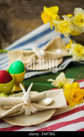 Spring festive easter dining table setting with yellow daffodil flowers,  napkins and vintage cutlery on a wooden board Stock Photo