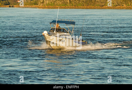 Small boat driven by recreational fisherman speeding across calm blue water of river estuary at Nambucca Heads NSW Australia Stock Photo