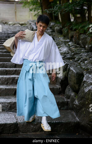 Japanese Shinto priest in traditional costume carrying a heavy bag down steps at The Grand Shrine, Ise (Ise Jingu), Japan. Inner Shrine; robe; robes Stock Photo