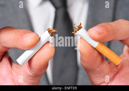 a man wearing a suit breaking a cigarette with his hands Stock Photo