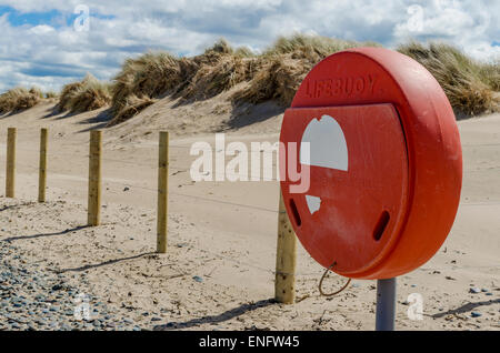 A lifebouy holder on a sandy and pebble strewn beach with sand dunes in the background Stock Photo