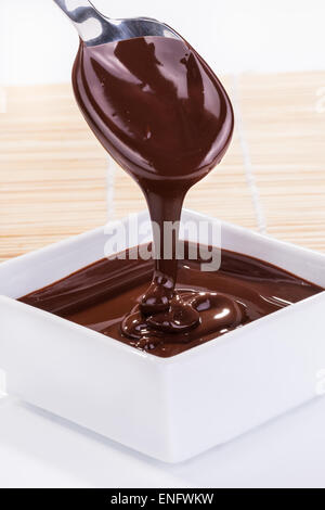 Chocolate sauce flows down from a spoon in to a bowl on a white table Stock Photo