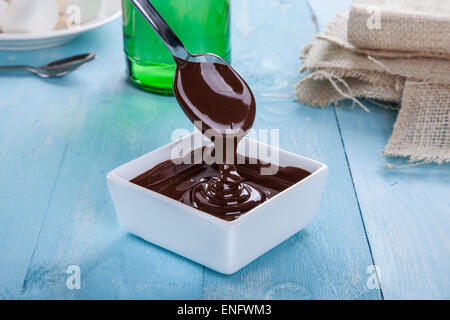 Chocolate sauce flows down from a spoon in to a bowl on a turquoise table Stock Photo