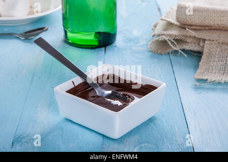 Chocolate sauce flows down from a spoon in to a bowl on a turquoise table Stock Photo