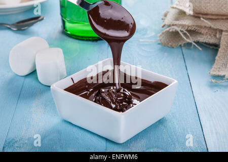Chocolate sauce flows down from a spoon in to a bowl on a turquoise table Stock Photo