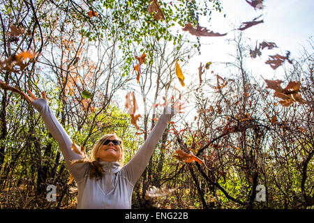 Caucasian woman throwing autumn leaves in forest Stock Photo