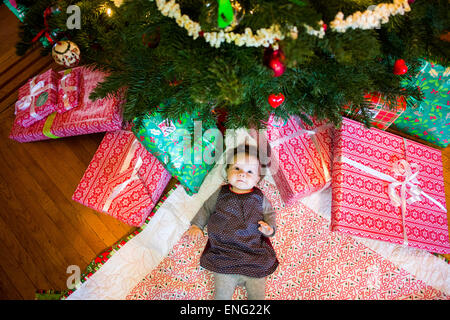 High angle view of Caucasian baby girl laying under Christmas tree Stock Photo