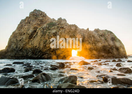 Sun shining through rock formation to ocean waves, Big Sur, California, United States Stock Photo