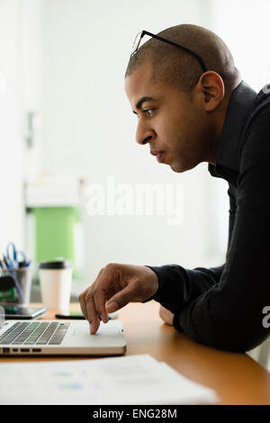 Mixed race businessman working on laptop at desk Stock Photo