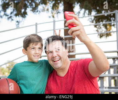Caucasian father and son taking cell phone photograph on bleachers Stock Photo