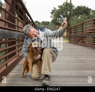 Caucasian man taking photograph with dog on bridge Stock Photo