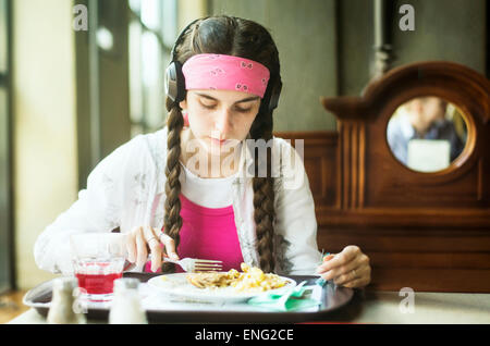 Caucasian woman wearing headphones eating in dining room Stock Photo