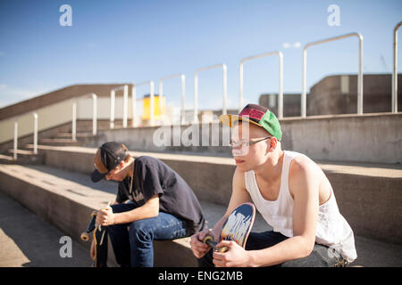 Caucasian men with skateboards sitting on steps Stock Photo