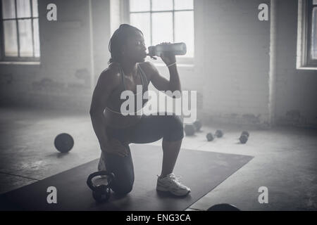 Black woman drinking water bottle in dark gym Stock Photo