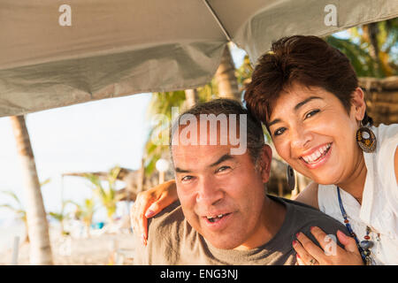 Hispanic couple smiling under umbrella on beach Stock Photo