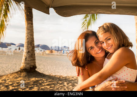 Mother and daughter hugging under umbrella on beach