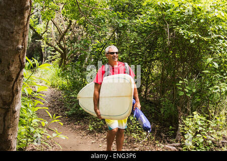 Caucasian man carrying surfboard in jungle Stock Photo